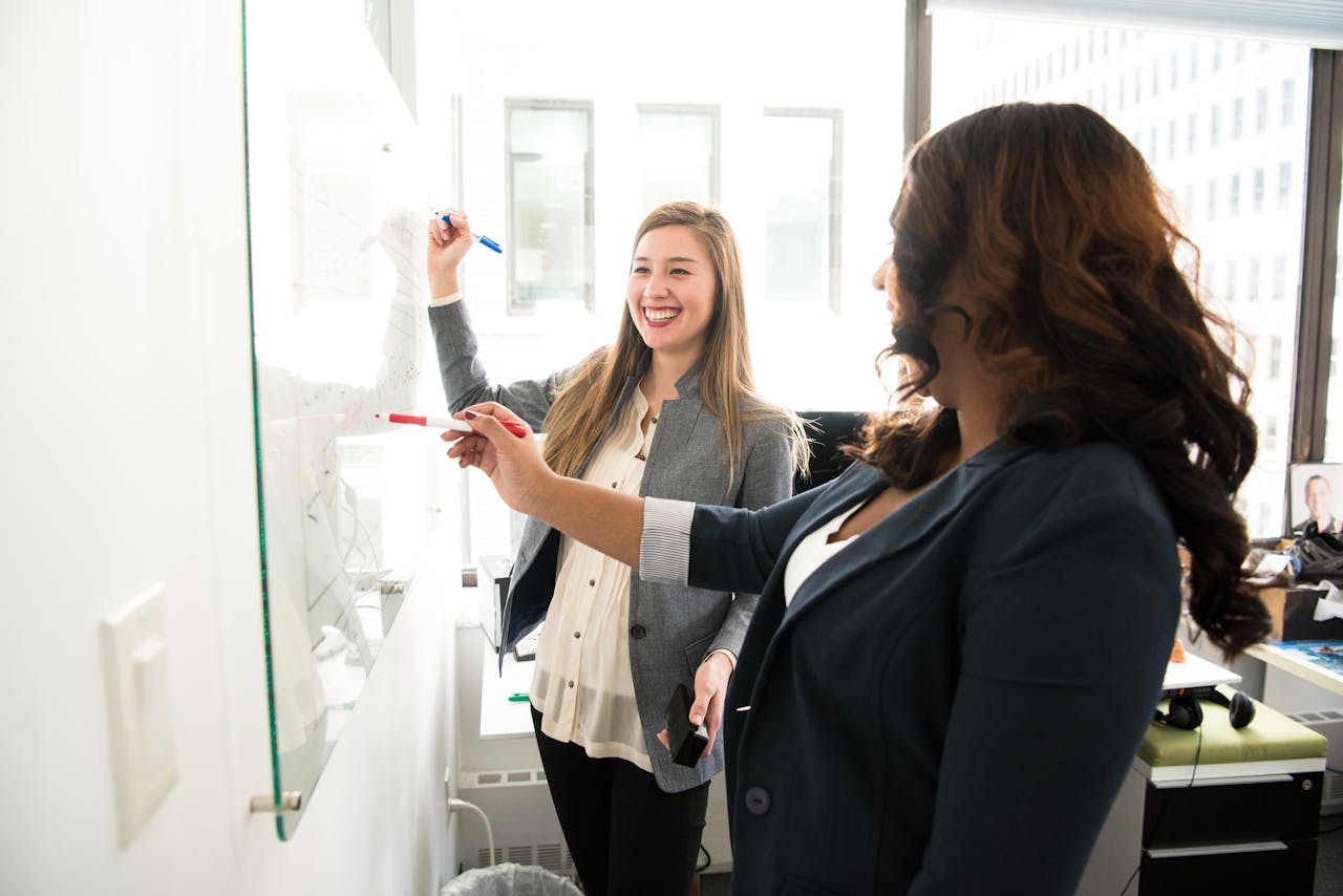 services-02 Two professional women discussing ideas on a whiteboard in a modern office setting.