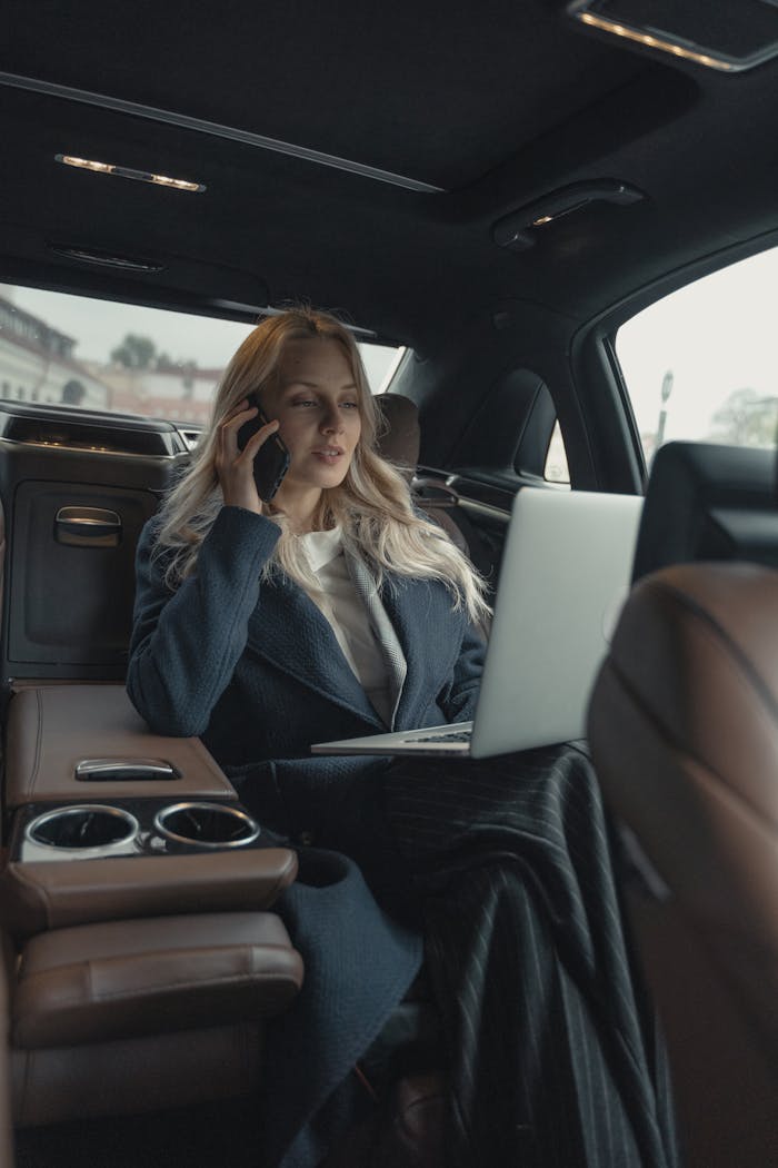 about-01 Confident businesswoman making a call and working on a laptop in a luxury car interior.