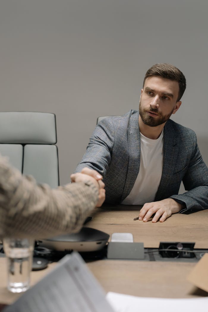 services-09 Two businessmen in a modern office shaking hands across a table. Professional setting.